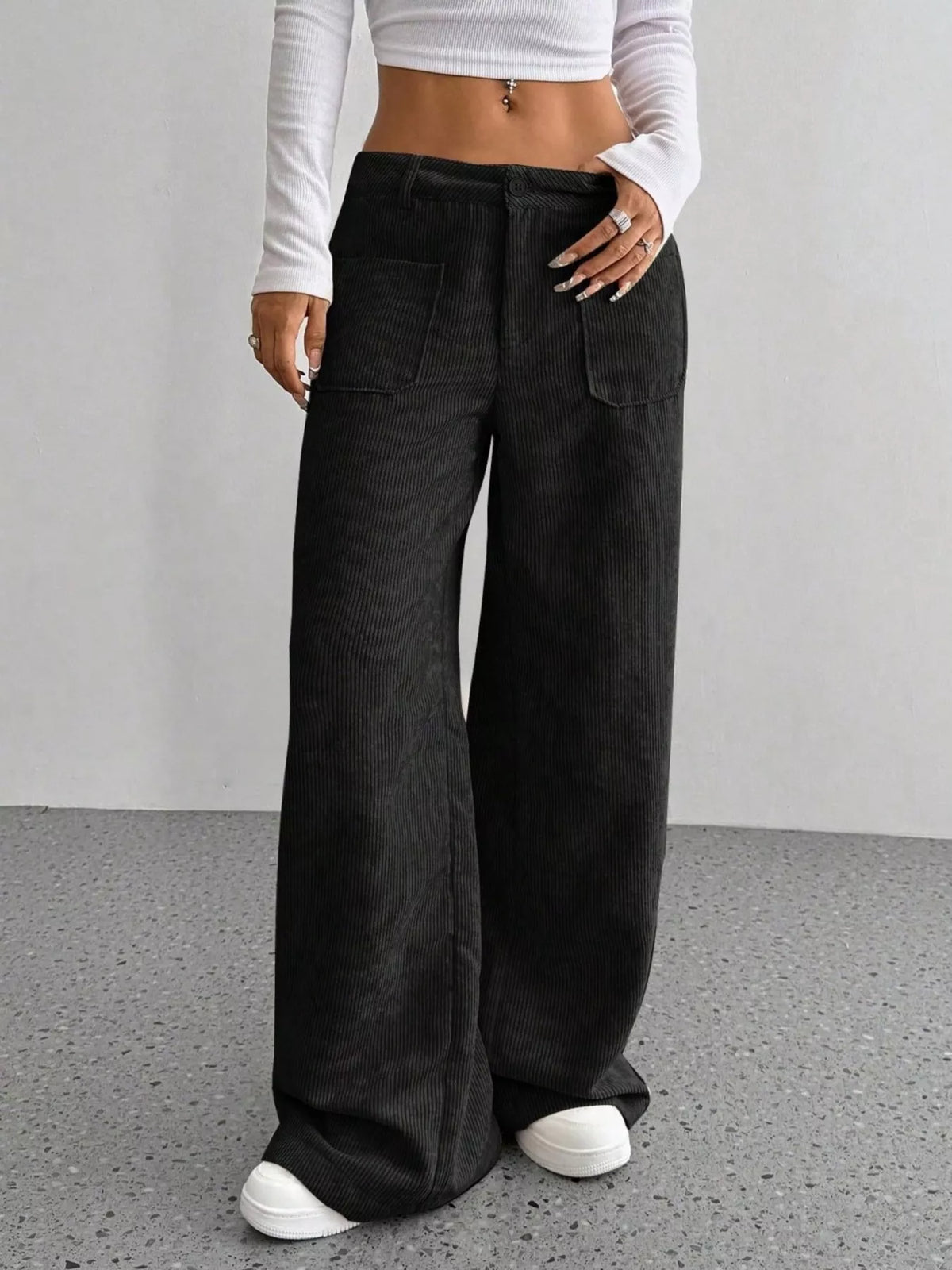 Black stretch corduroy wide-leg pants featuring front patch pockets, a button-zip fly, and a relaxed floor-length fit.