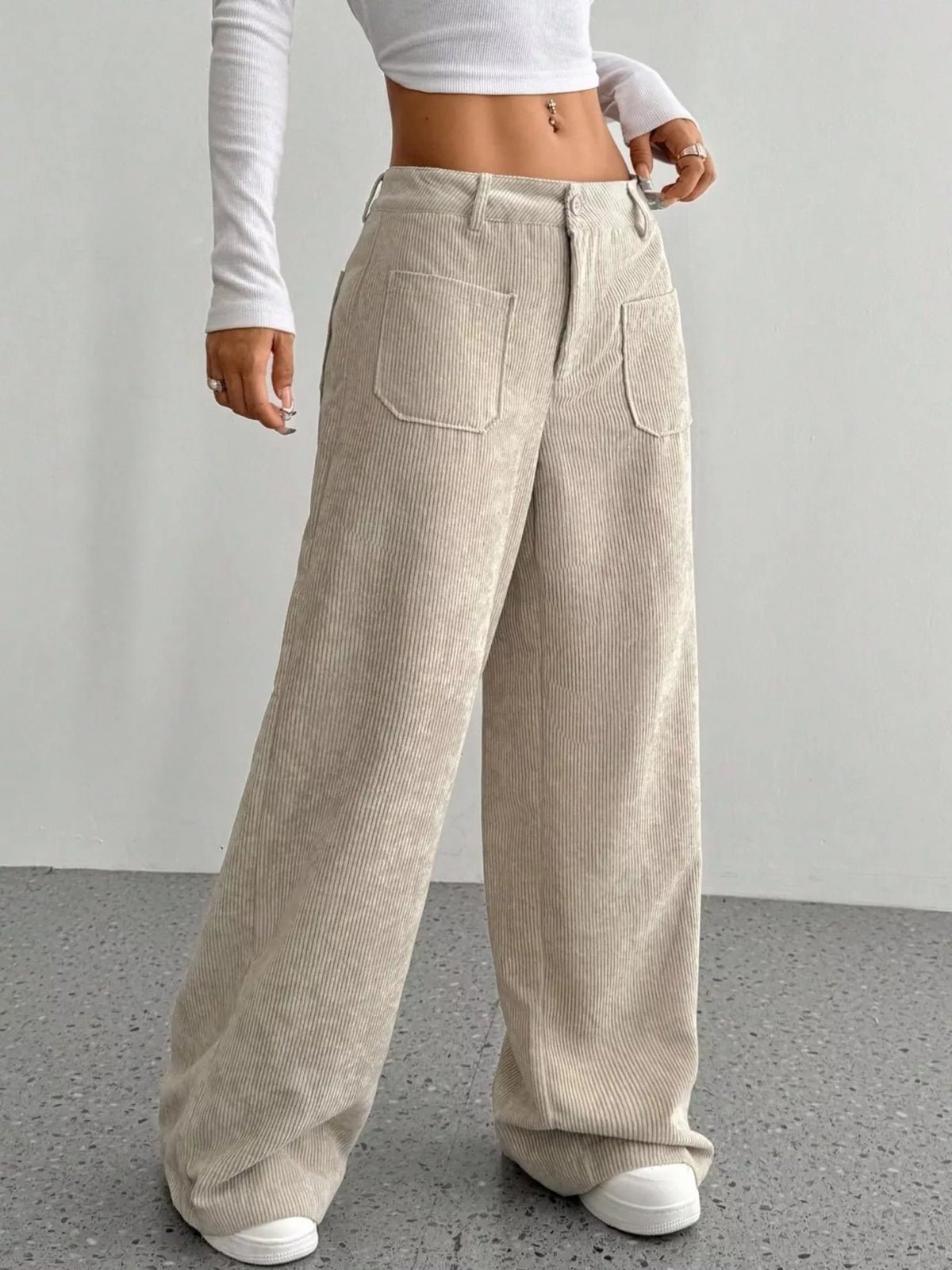 Beige stretch corduroy wide-leg pants featuring front patch pockets, a mid-rise waist, and a clean button-zip fly.