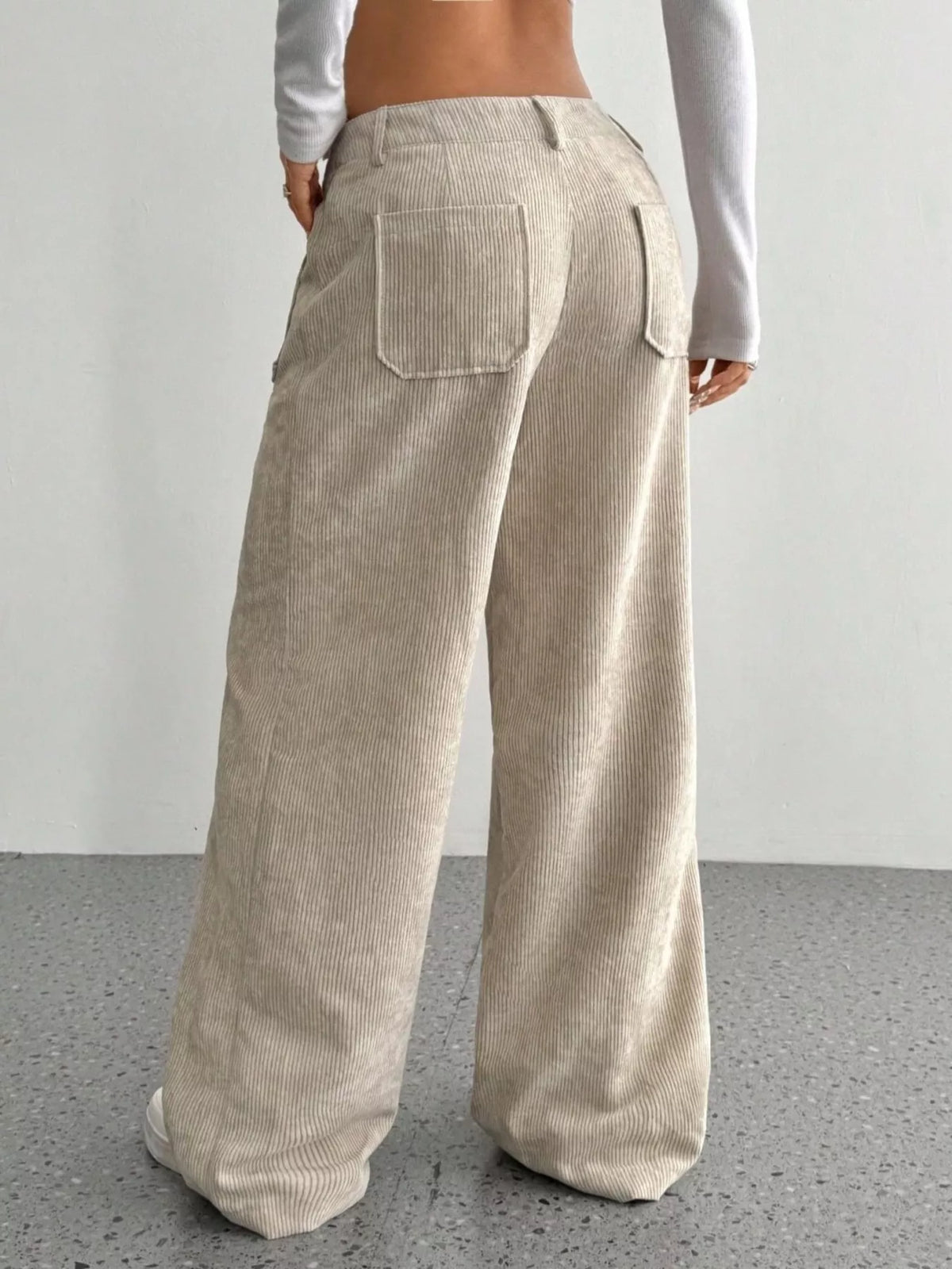 Beige stretch corduroy wide-leg pants featuring back patch pockets and a mid-rise fit, shown from behind.