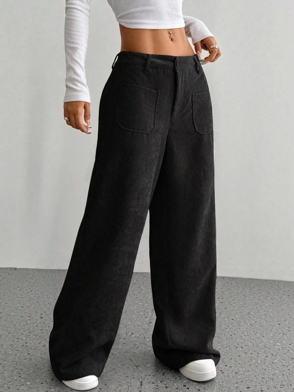 Black stretch corduroy wide-leg pants featuring front patch pockets, a button-zip fly, and a relaxed, floor-length silhouette.
