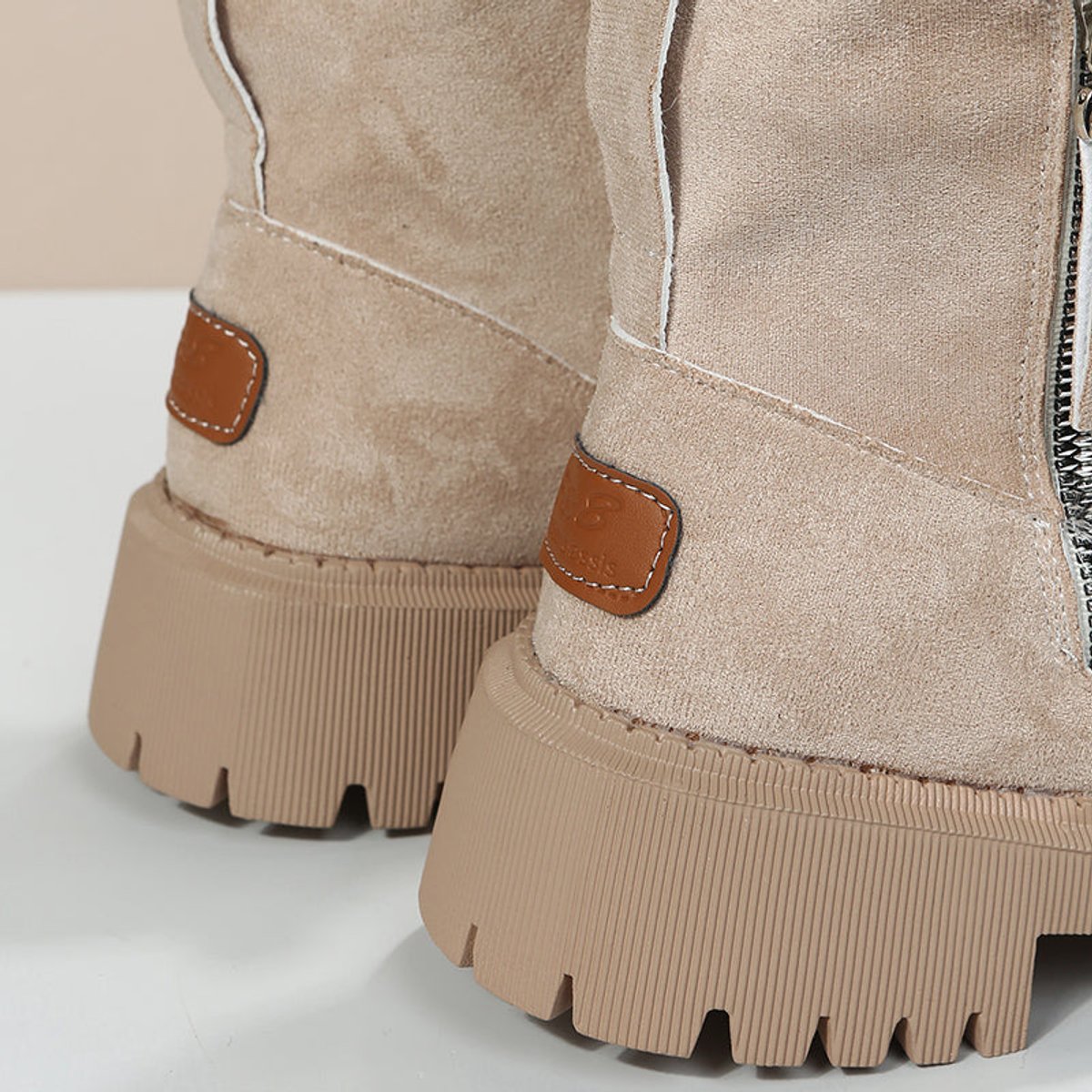 Detail of a beige suede platform boot showing the leather tab, side zip and chunky platform edge
