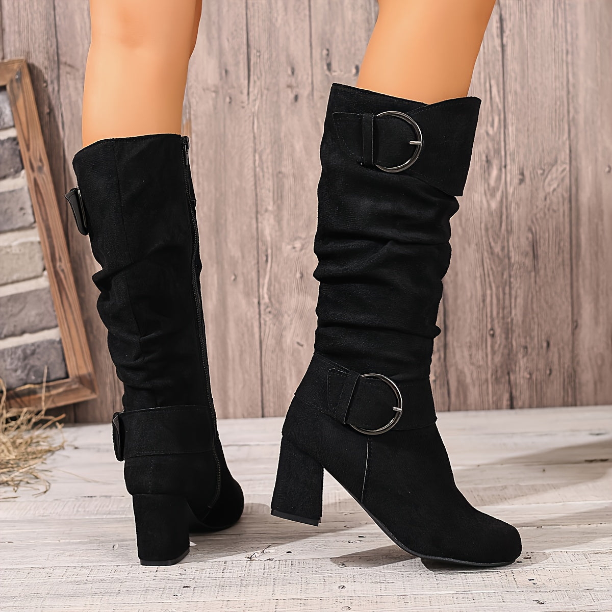 Black suede knee-high boots with a ruched slouch shaft, fold-over cuff, twin ring buckles, and a sturdy block heel.