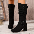 Black suede slouch knee-high boots with ruched shafts, fold-over cuffs, twin ring buckles, and a sturdy block heel.