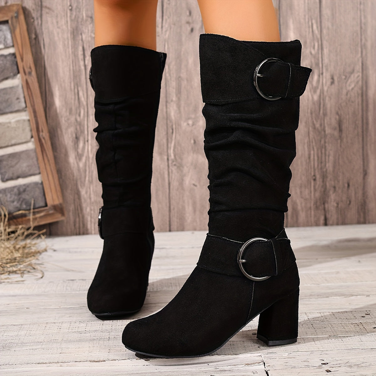 Black suede slouch knee-high boots with ruched shafts, fold-over cuffs, twin ring buckles, and a sturdy block heel.