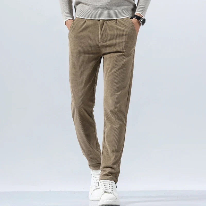 Taupe heavyweight corduroy pants in a straight-leg fit with a clean zip-fly, worn with a grey sweater and white sneakers.