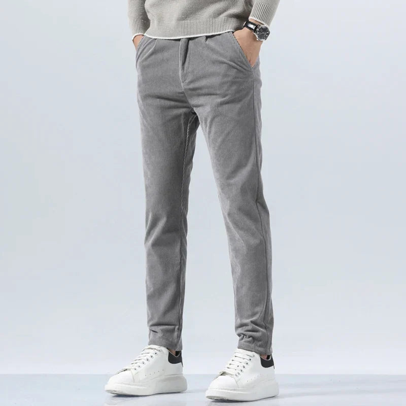 Gray straight-fit corduroy pants in heavyweight cotton with a clean zip-fly, worn with a sweater and white sneakers.
