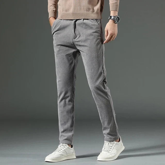 Gray heavyweight corduroy pants in a straight-leg fit with a clean zip-fly, styled with a beige sweater and white sneakers.