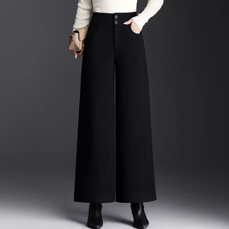 Front view of a model wearing high-waisted black tailored wide-leg wool trousers with double-button waistband detail, styled with a white top and black boots.
