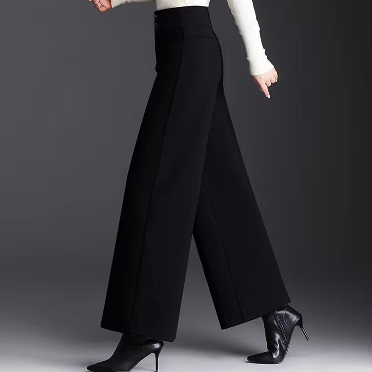 Side profile view of a model walking in high-waisted black wide-leg wool trousers paired with black heeled ankle boots.