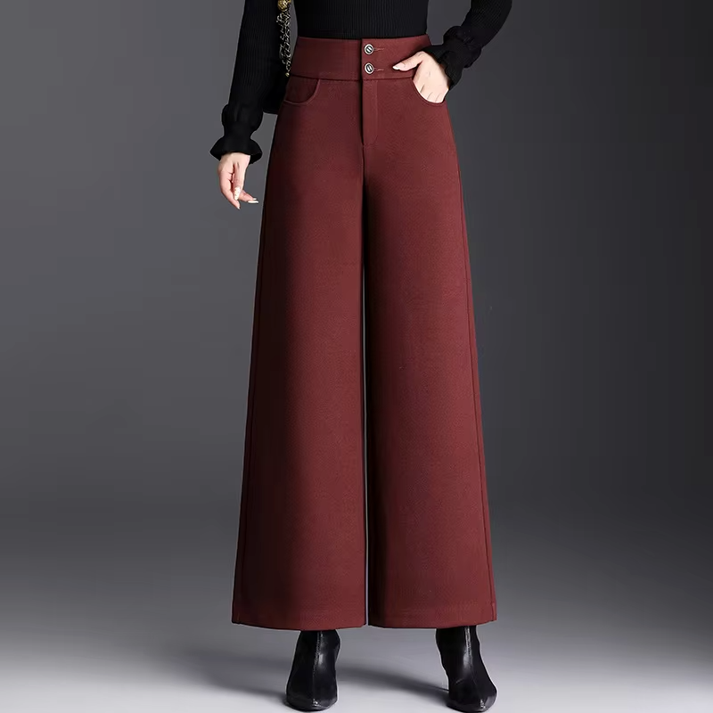 Front view of a model wearing high-waisted burgundy red tailored wide-leg wool trousers with double-button waistband and side pockets.