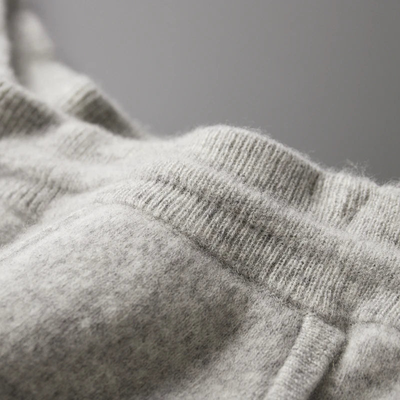 Close-up of light gray wool knit trousers featuring a soft, textured fabric and a ribbed elastic waistband.