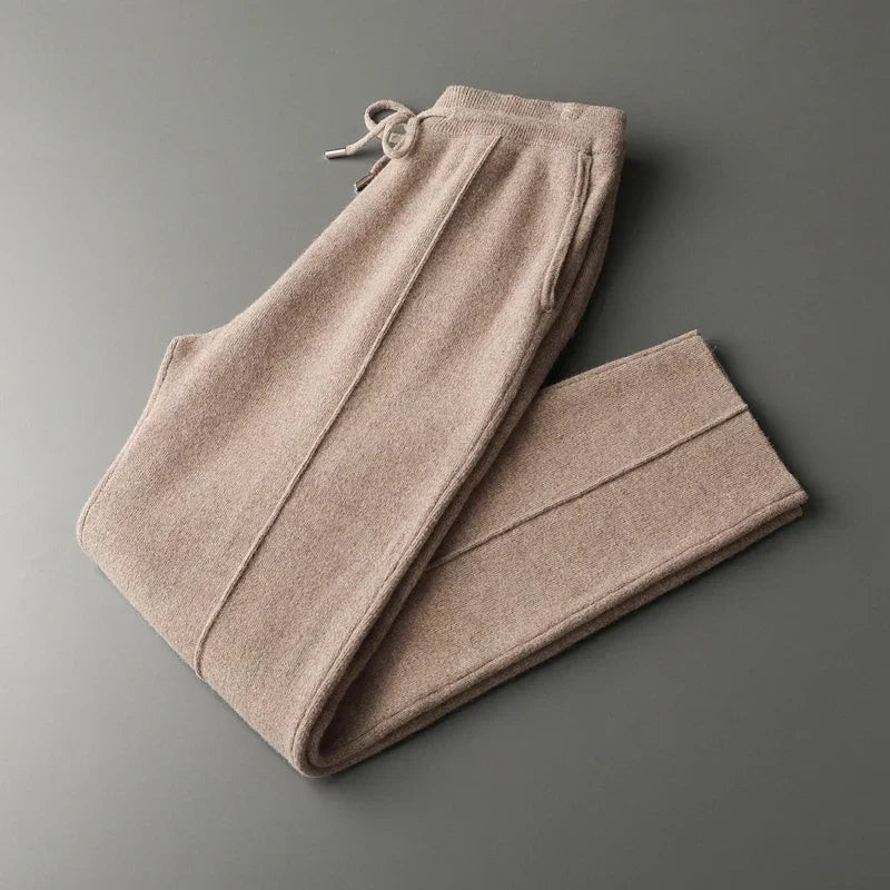 Beige wool knit trousers featuring a relaxed tapered fit, drawstring waist, and center-seam detailing on a gray background.