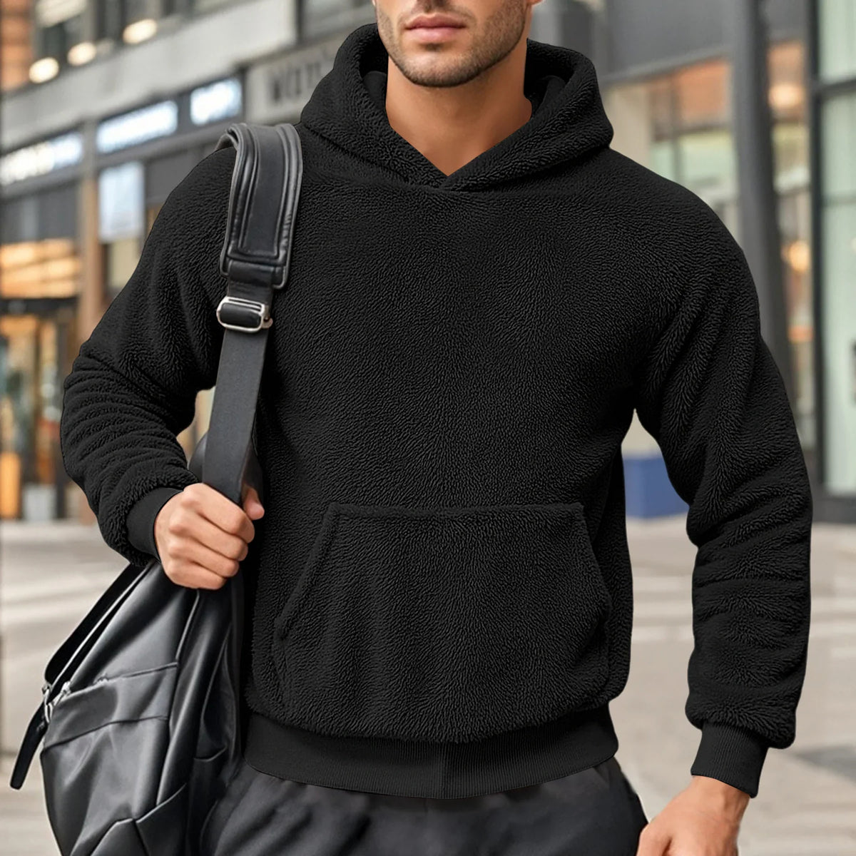 Black teddy fleece hoodie worn by a male model, shown from the front with a shoulder bag.