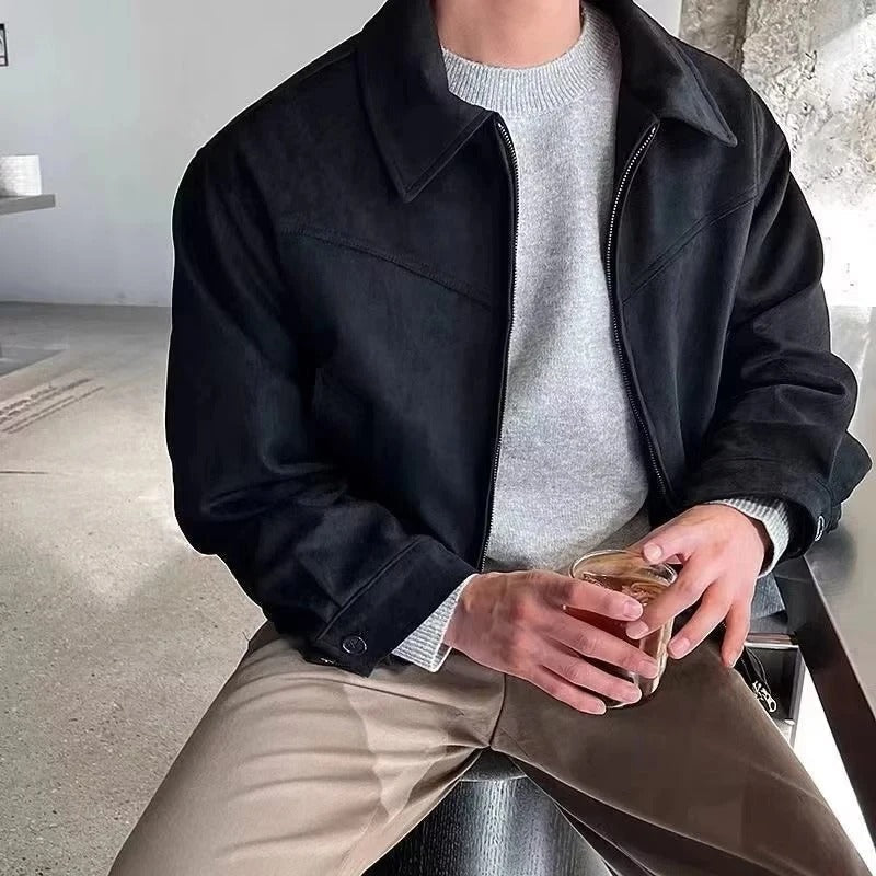 Black suede bomber jacket with a point collar, zip-front closure, and buttoned cuffs worn over a grey knit sweater.