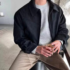 Black suede bomber jacket with a point collar, zip-front closure, and buttoned cuffs worn over a grey knit sweater.