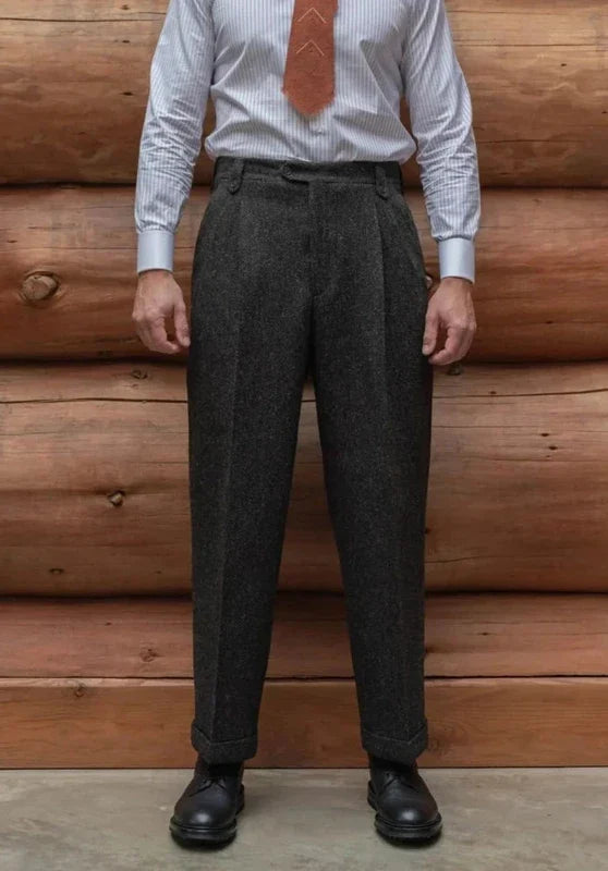 Black wool tweed trousers featuring a flat-front, straight-leg silhouette and cuffed hems against a wood background.