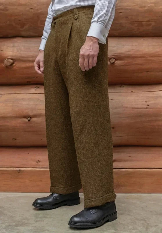 Khaki tweed wool trousers featuring a straight-leg fit, flat front, and cuffed hems against a rustic log wall.