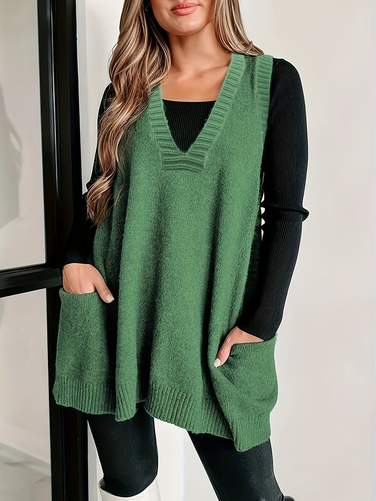 Front view of a model with hands in pockets wearing the fuzzy V-neck knit sweater vest in sage green with front patch pockets over a black long-sleeve shirt.