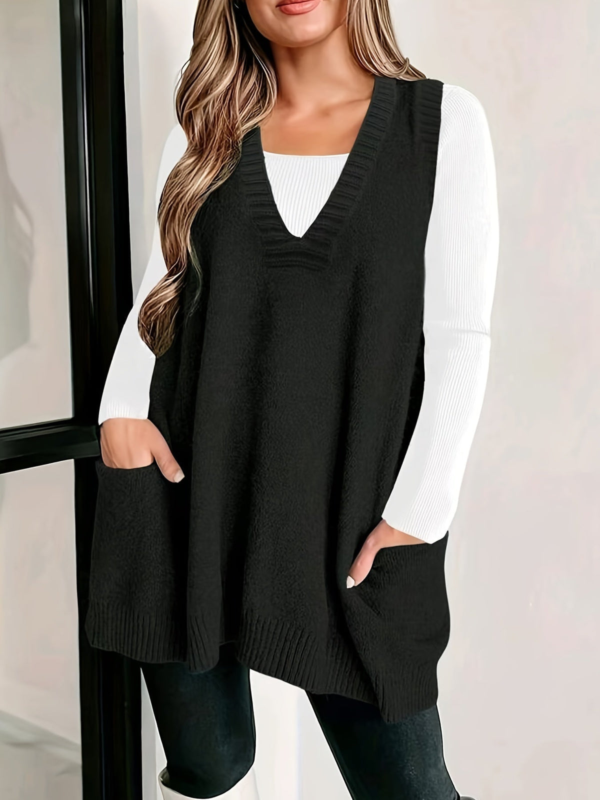 Front view of a model with hands in pockets wearing the fuzzy V-neck knit sweater vest in classic black layered over a white long-sleeve top.