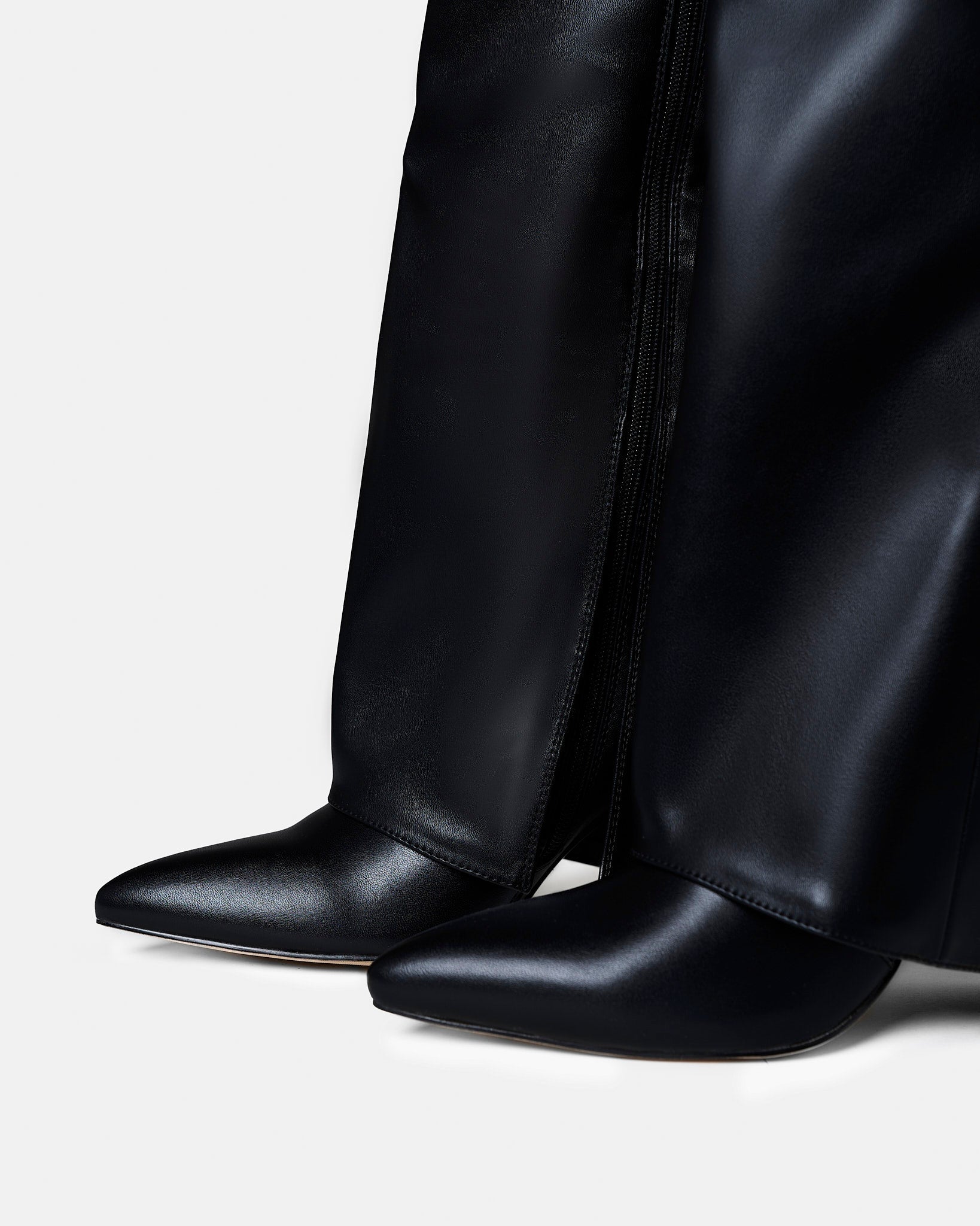 Close-up of black knee-high leather riding boots highlighting the pointed toe, smooth leather finish, and low block heel.