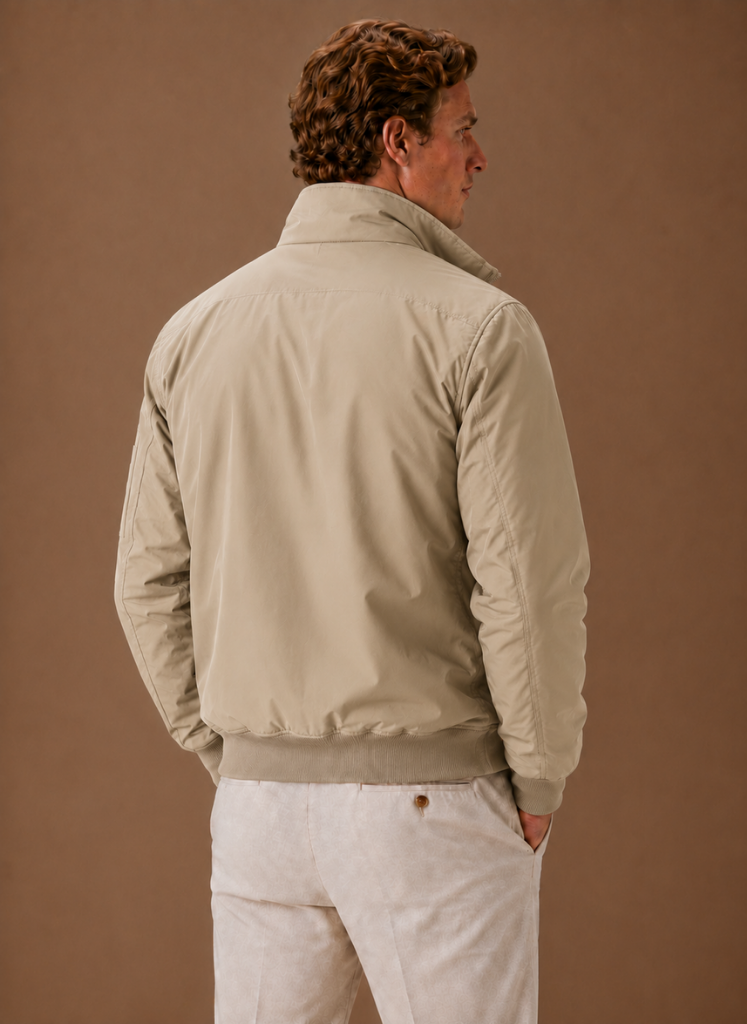 Back view of a man wearing a khaki utility bomber jacket with a stand collar and ribbed hem.