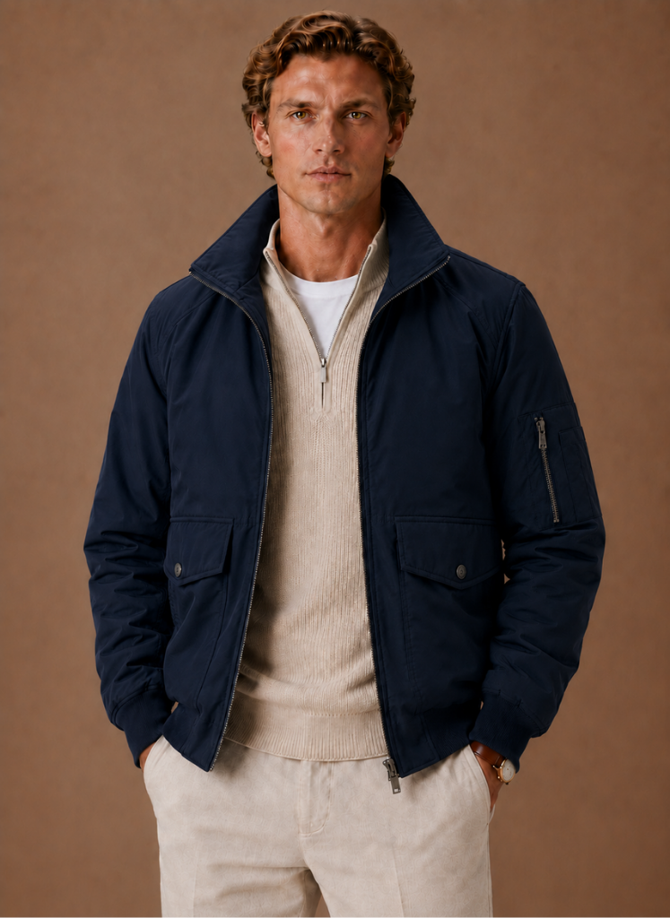Man wearing a navy utility bomber jacket over a cream knit sweater and light-colored trousers.
