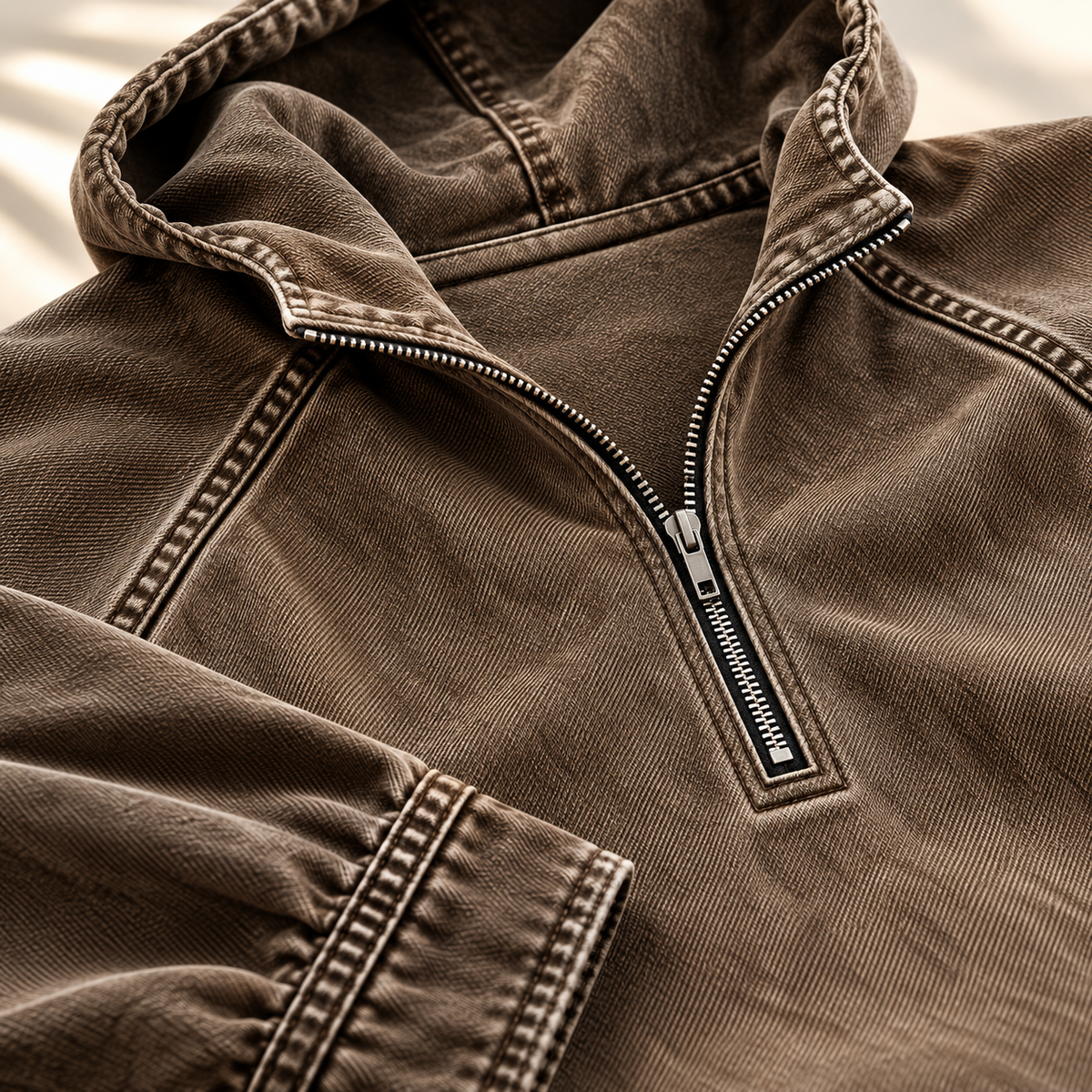 Close-up of the brown hoodie showing the half-zip collar, raglan seam, and contrast topstitching.