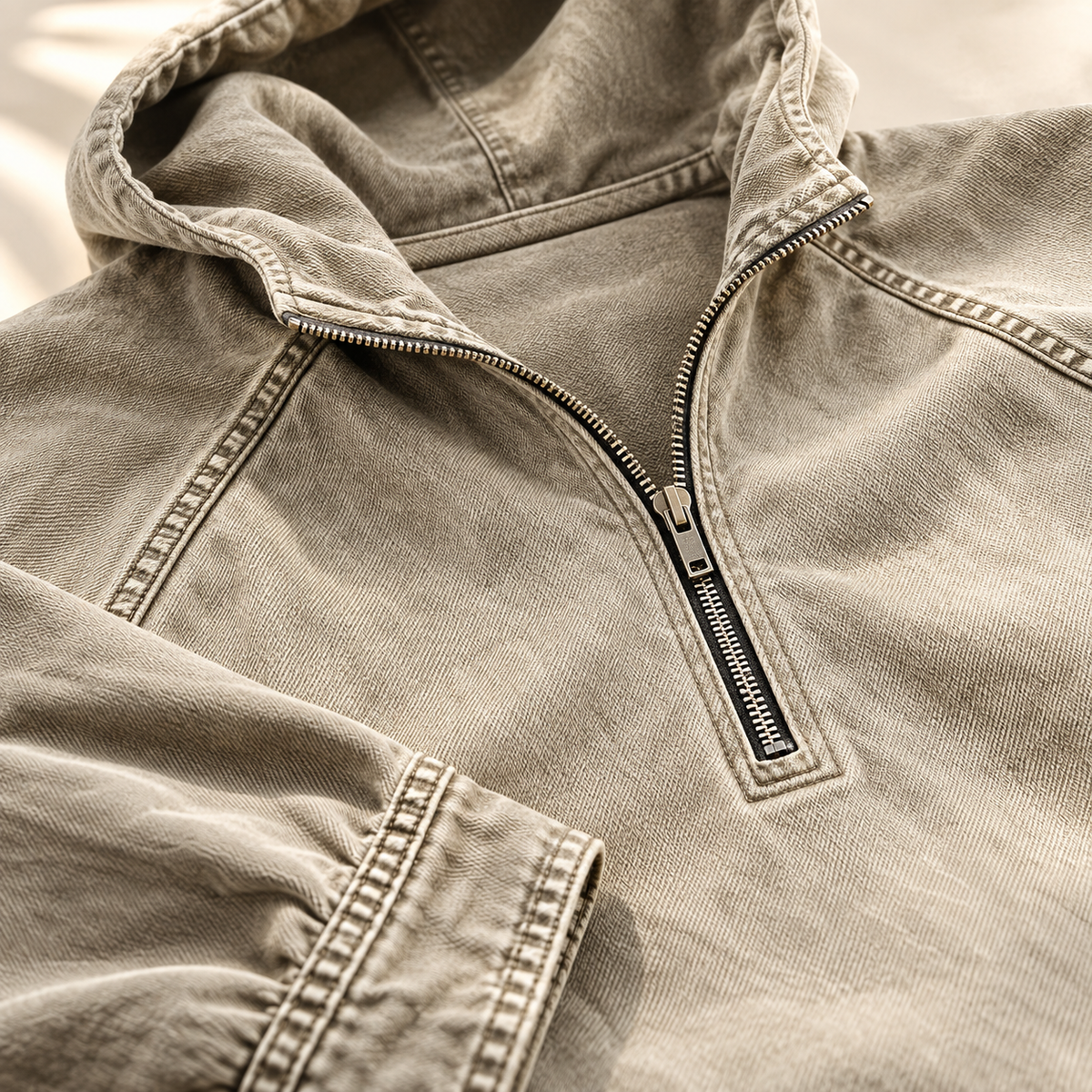 Close-up of the beige hoodie showing the half-zip collar and contrast topstitching.