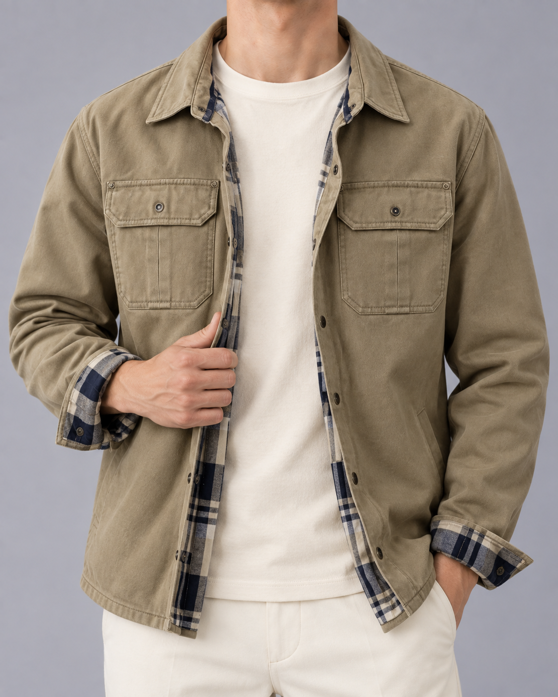Front view of a model wearing the khaki waxed cotton jacket with an open snap front, dual chest pockets, and patterned plaid inner lining exposed at the cuffs.