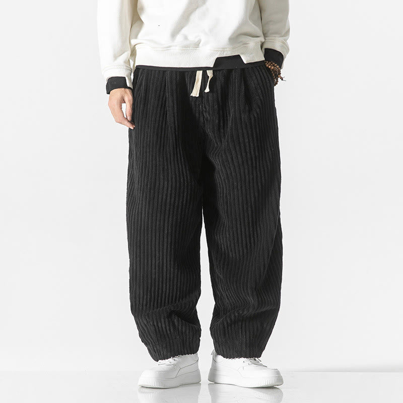 Black wide-wale corduroy harem pants featuring a drawstring waist, roomy seat, and tapered ankles worn with white sneakers.
