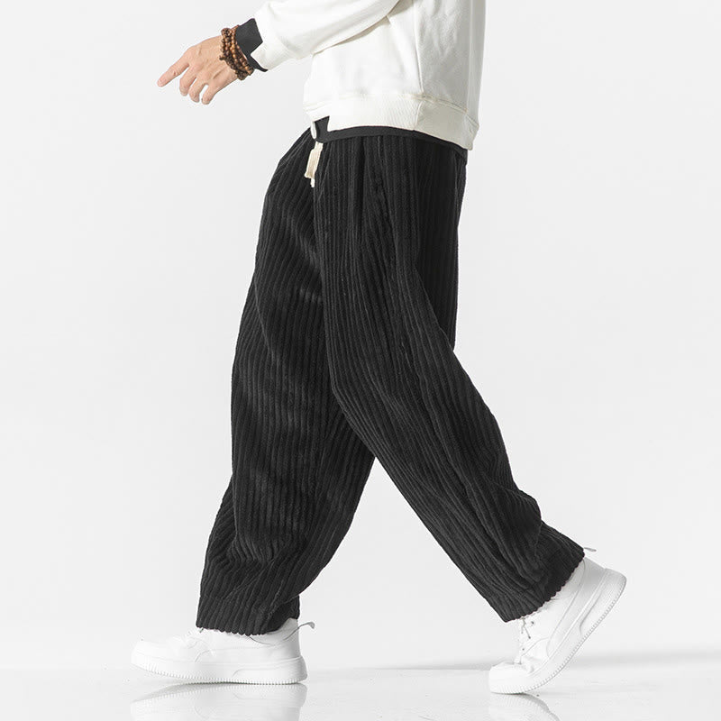 Black wide-wale corduroy harem pants with a drawstring waist, relaxed fit, and tapered ankles worn with white sneakers.