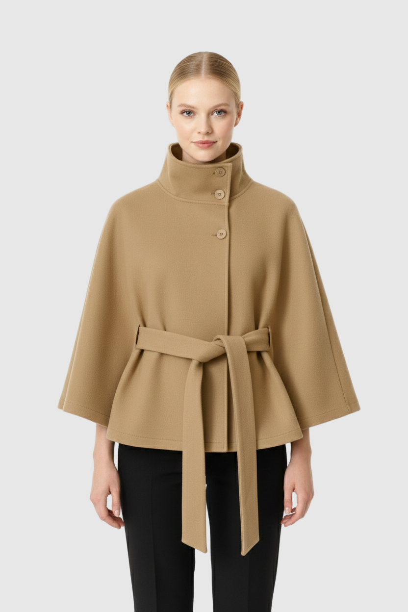Front view of a model wearing a camel  belted wool cape coat with a stand collar and wide cape sleeves, paired with black pants.