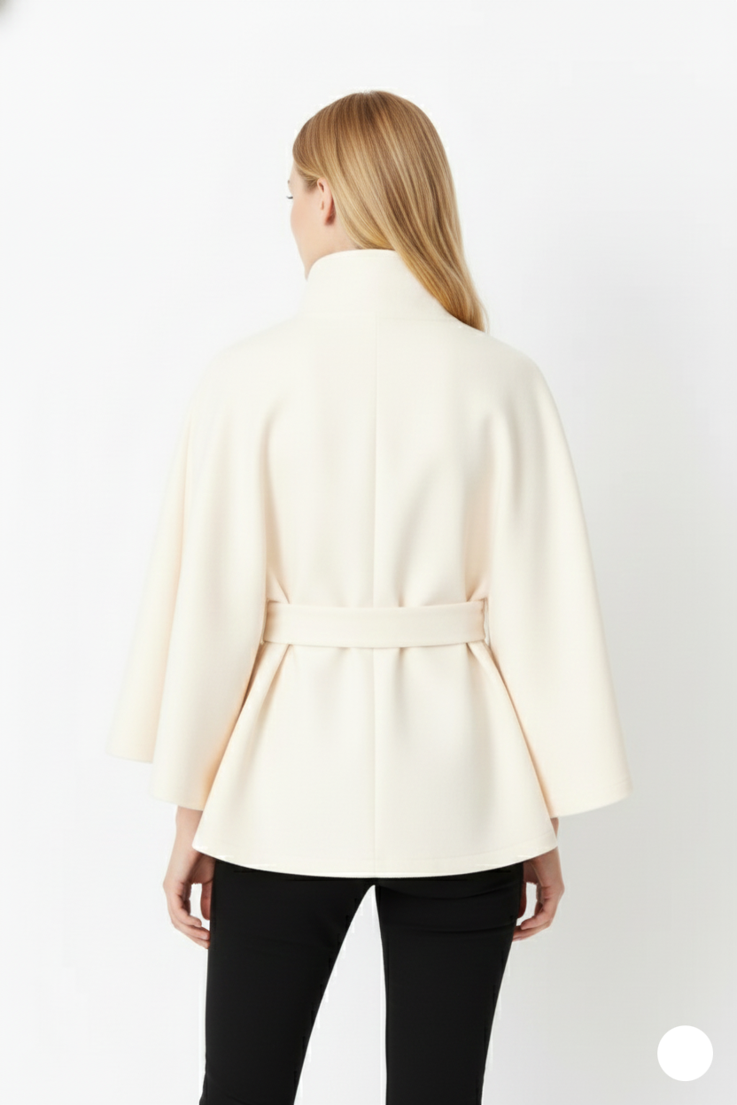 Back view of a model wearing a cream wool cape coat, highlighting the clean silhouette and tied waist belt.