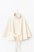 Cream wool-blend cape coat hanging on a hanger featuring a high stand collar, asymmetrical front button closure, wide flared cape sleeves, and a matching tie waist belt.