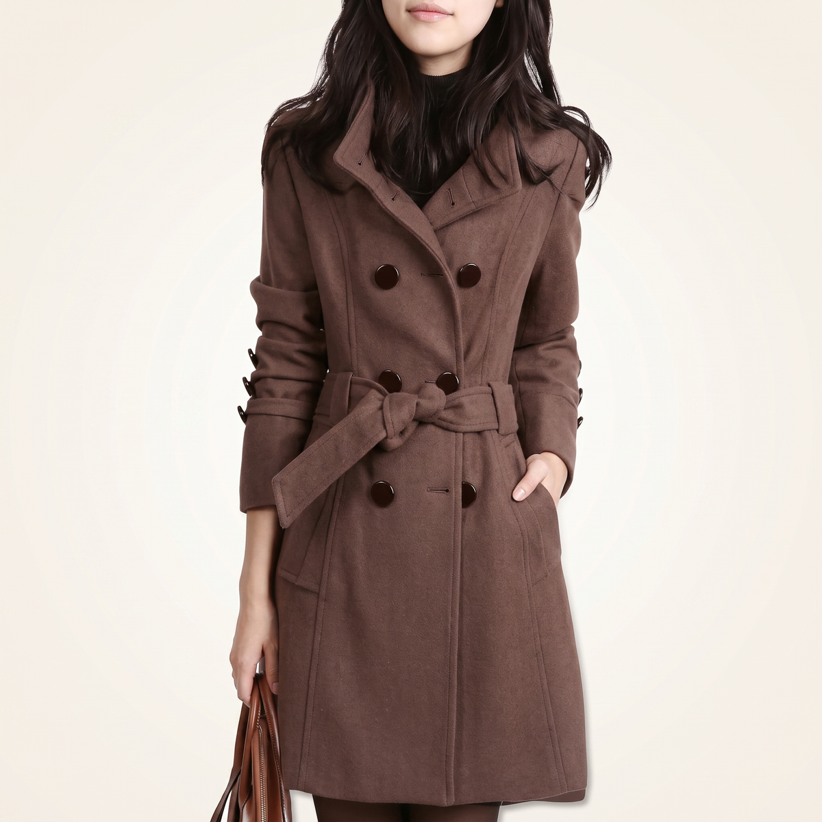 Woman wearing a brown double-breasted wool-blend trench coat featuring a high collar, waist belt tied in a knot, sleeve cuff tab details, and side pockets, holding a brown handbag.