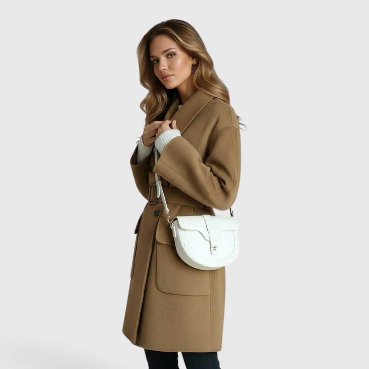 Woman wearing a camel tan knee-length wool-blend double-breasted coat with wide lapels and front flap pockets, carrying a white cross-body bag.
