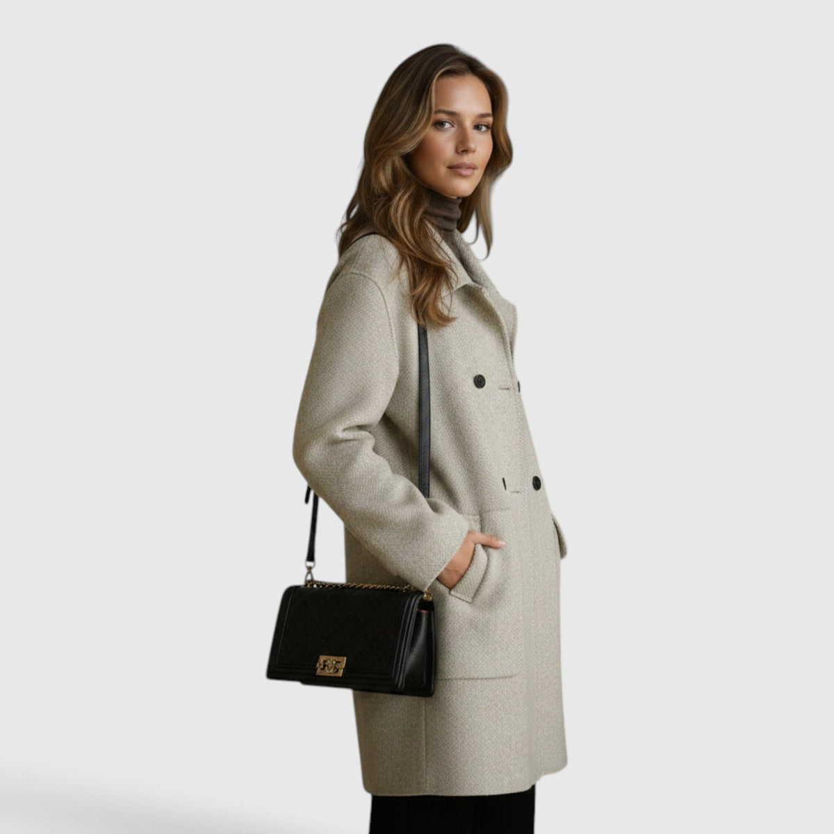 Side view of a woman wearing a light beige knee-length wool-blend coat with a black shoulder bag.