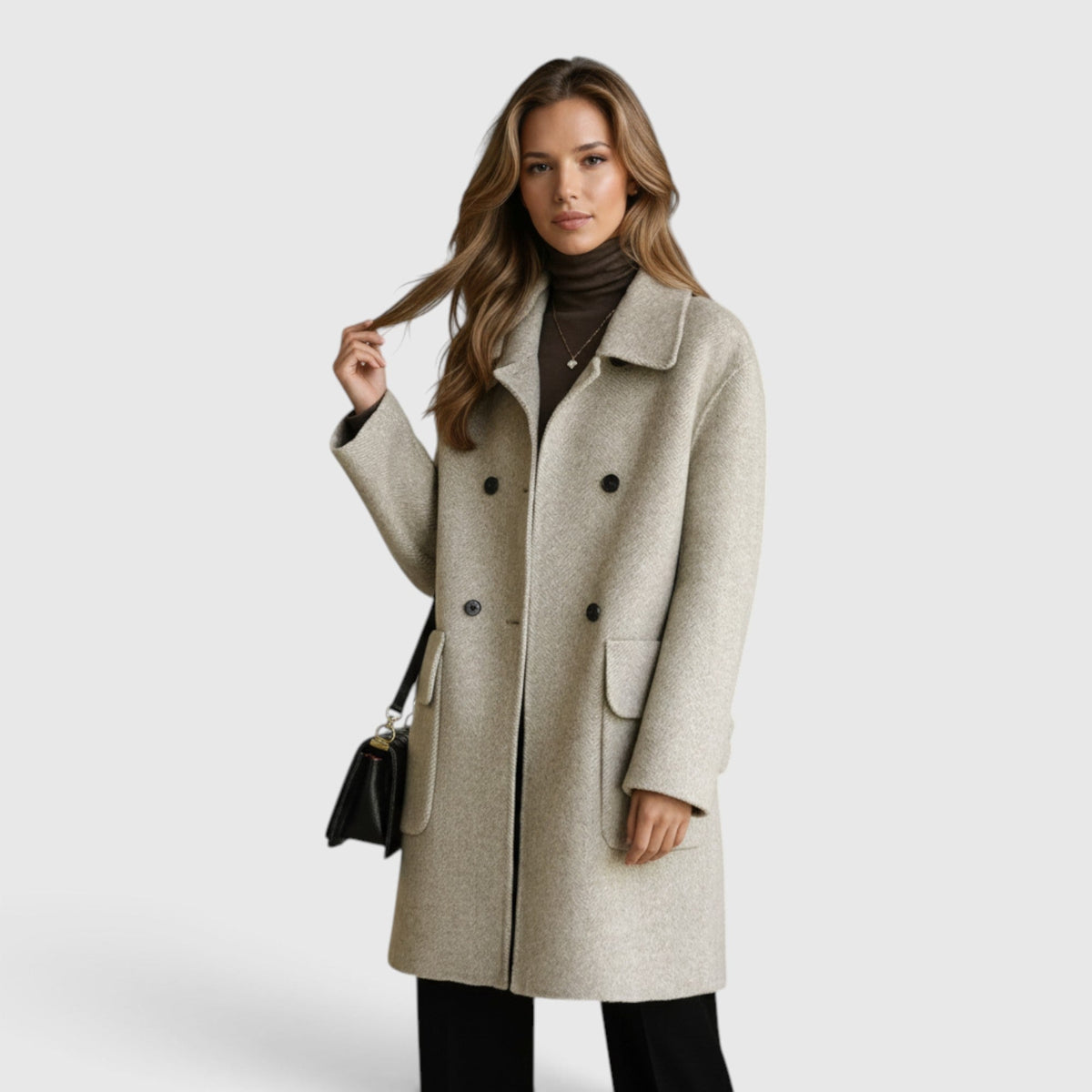 Woman wearing a light beige or oatmeal knee-length wool-blend coat styled over a dark brown turtleneck sweater and dark trousers, holding a black shoulder bag.