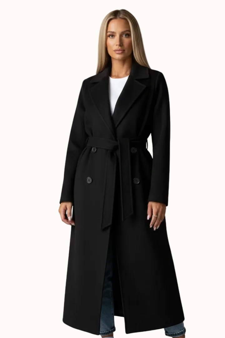Front view of a woman wearing an ankle-length black double-breasted coat with wide notch lapels and a tied waist belt.