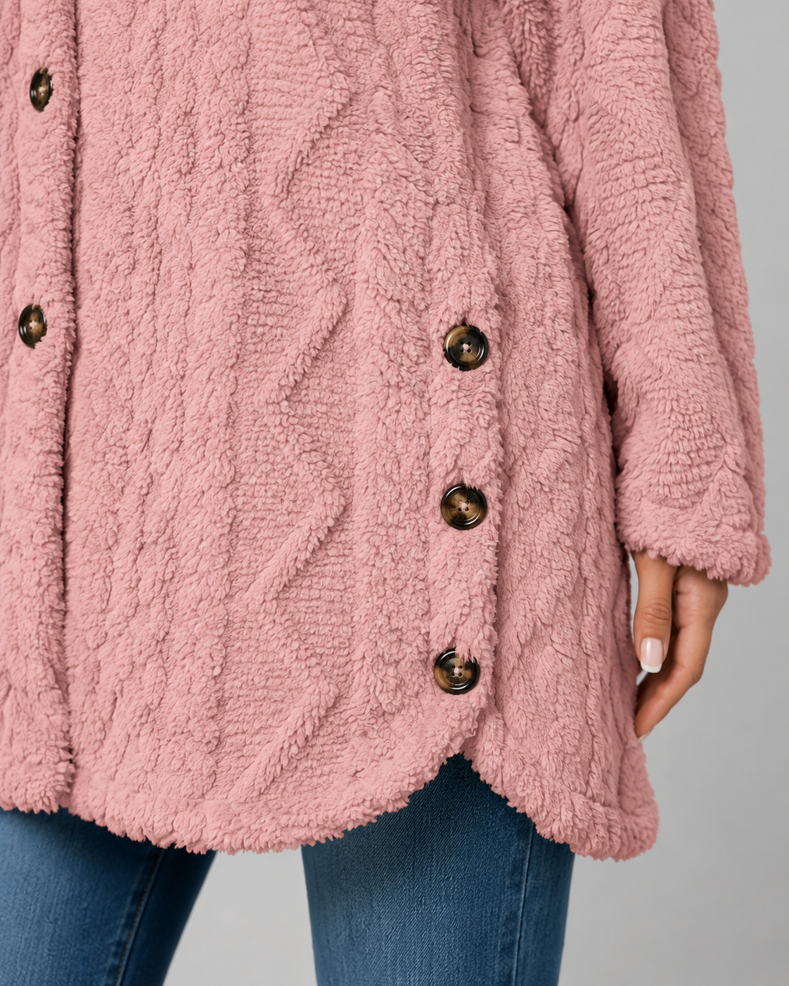 Close-up view of the lower side seam of a dusty rose pink cable-textured teddy fleece jacket showing side buttons and a rounded hem.