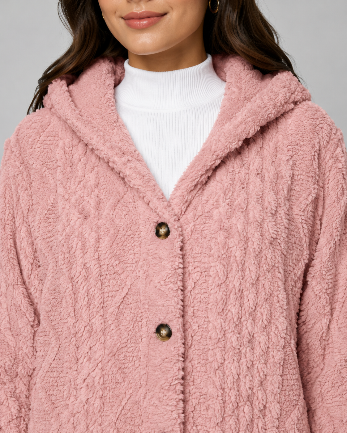 Close-up front view of a woman wearing a dusty rose pink hooded teddy fleece jacket with front button closures and a white turtleneck.