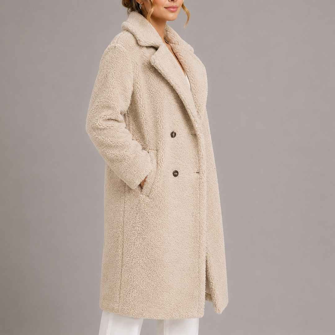 Three-quarter side profile of a model in a cream-colored longline teddy coat with hands in side pockets.