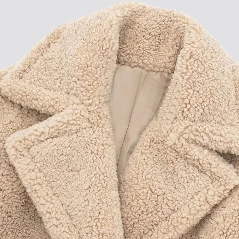 Close-up shot showing the textured faux-fur fabric, smooth lining, and structured notch lapel collar of the cream teddy coat.