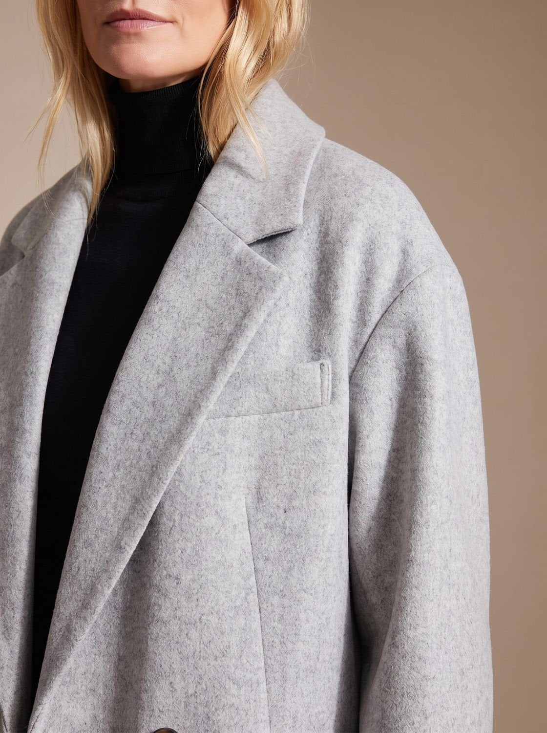 Close-up shot of the wide notch lapel collar, chest welt pocket, and shoulder structure of the light grey oversized overcoat.