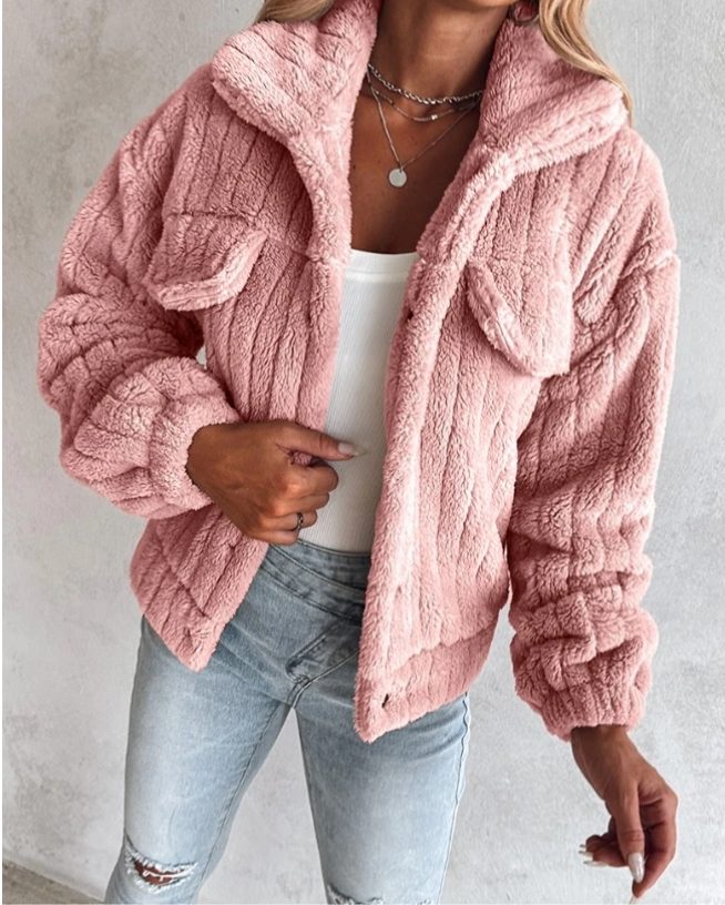 A woman wearing a dusty pink oversized teddy fleece jacket with chest pockets, styled over a white top and light jeans.