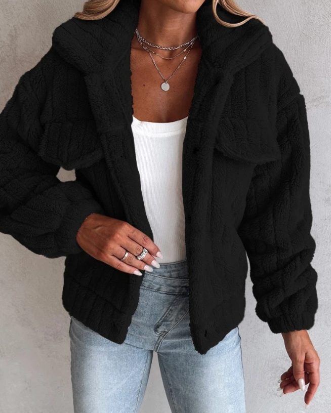 A woman wearing a black oversized teddy fleece jacket with flap pockets, layered over a white top and blue jeans.