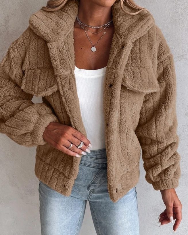 A woman wearing a warm brown oversized teddy fleece jacket with flap chest pockets, paired with a white top and jeans.