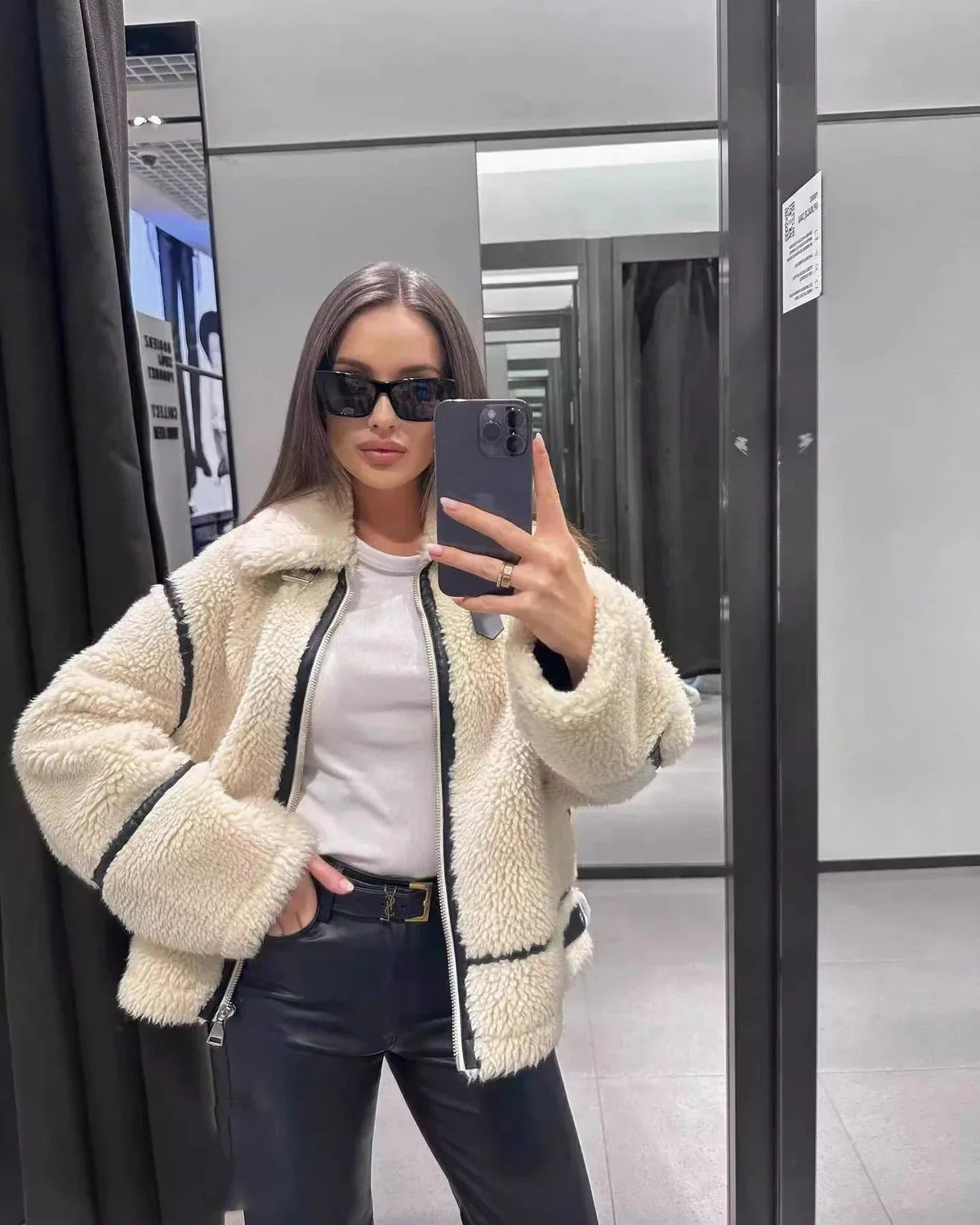 A woman taking a mirror selfie wearing the cream-and-black contrast trim teddy jacket open over a white t-shirt and dark jeans.