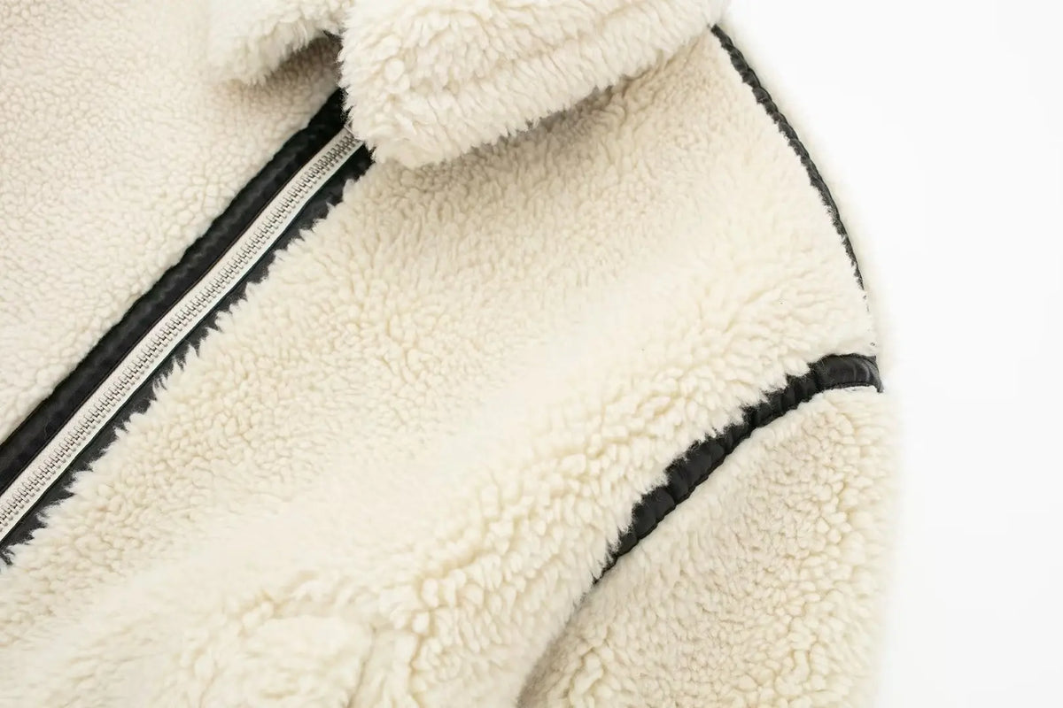 Close-up detail of the collar, zip front, and black piped seam detailing on the shoulder of the cream fleece jacket.