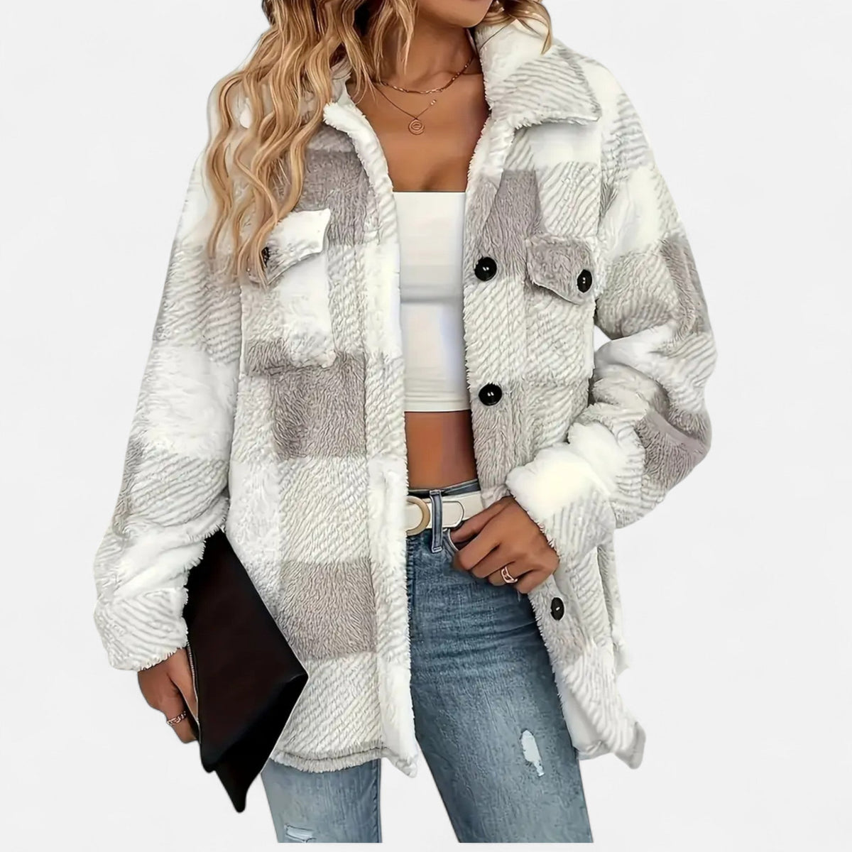 A woman wearing a white-and-light-grey buffalo plaid teddy fleece jacket open over a white crop top and blue jeans, holding a black clutch bag.